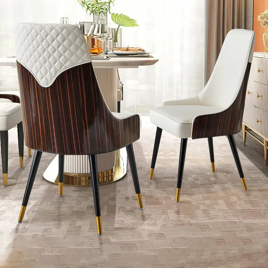 Two dining chairs in a modern interior. The left chair has a walnut back with a quilted white faux leather design, while the right chair is fully upholstered in white with black legs and gold accents. A dining table is visible in the background.
